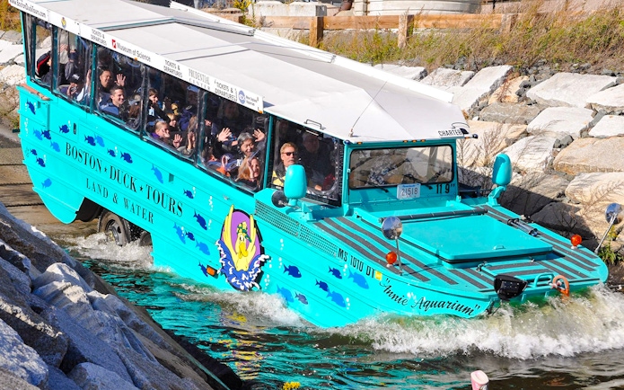 Boston Duck Tours amphibious vehicle entering water with passengers waving.