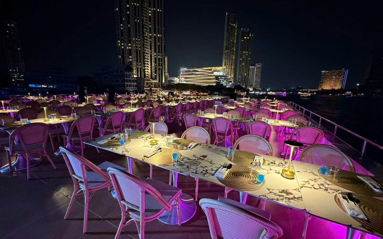 Dining setup on Super Galaxy Luxury Chao Phraya River Dinner Cruise with city skyline.