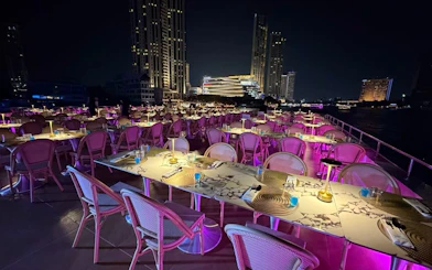 Dining setup on Super Galaxy Luxury Chao Phraya River Dinner Cruise with city skyline.