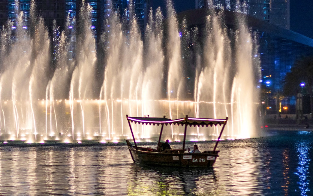 Traditional abra boat on Dubai Lake with fountain show at night.