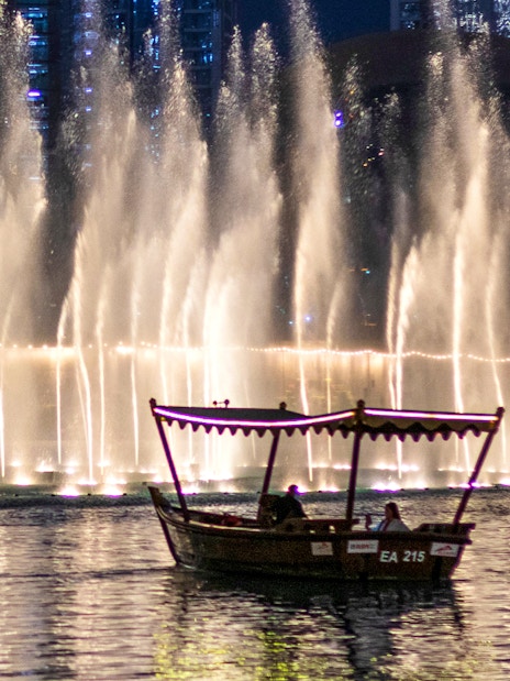 Traditional abra boat on Dubai Lake with fountain show at night.