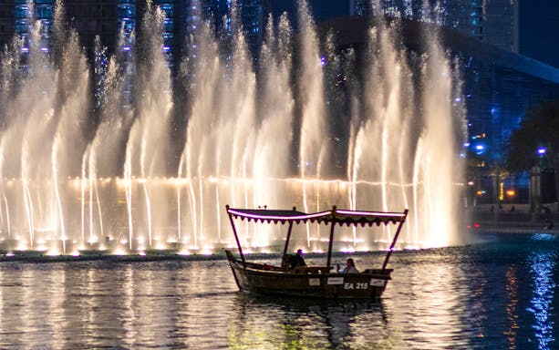 Traditional abra boat on Dubai Lake with fountain show at night.