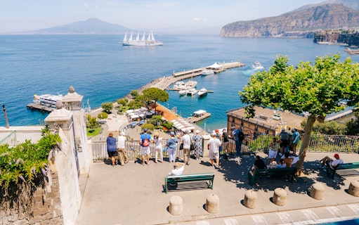 Tourists overlooking Marina Piccola in Sorrento with boats and Mount Vesuvius in the background.