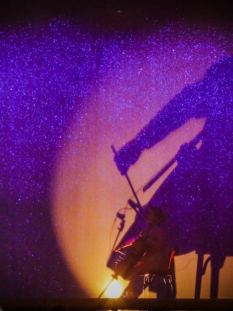 Performer singing with shadow of cellist at Paradis Latin festive show.