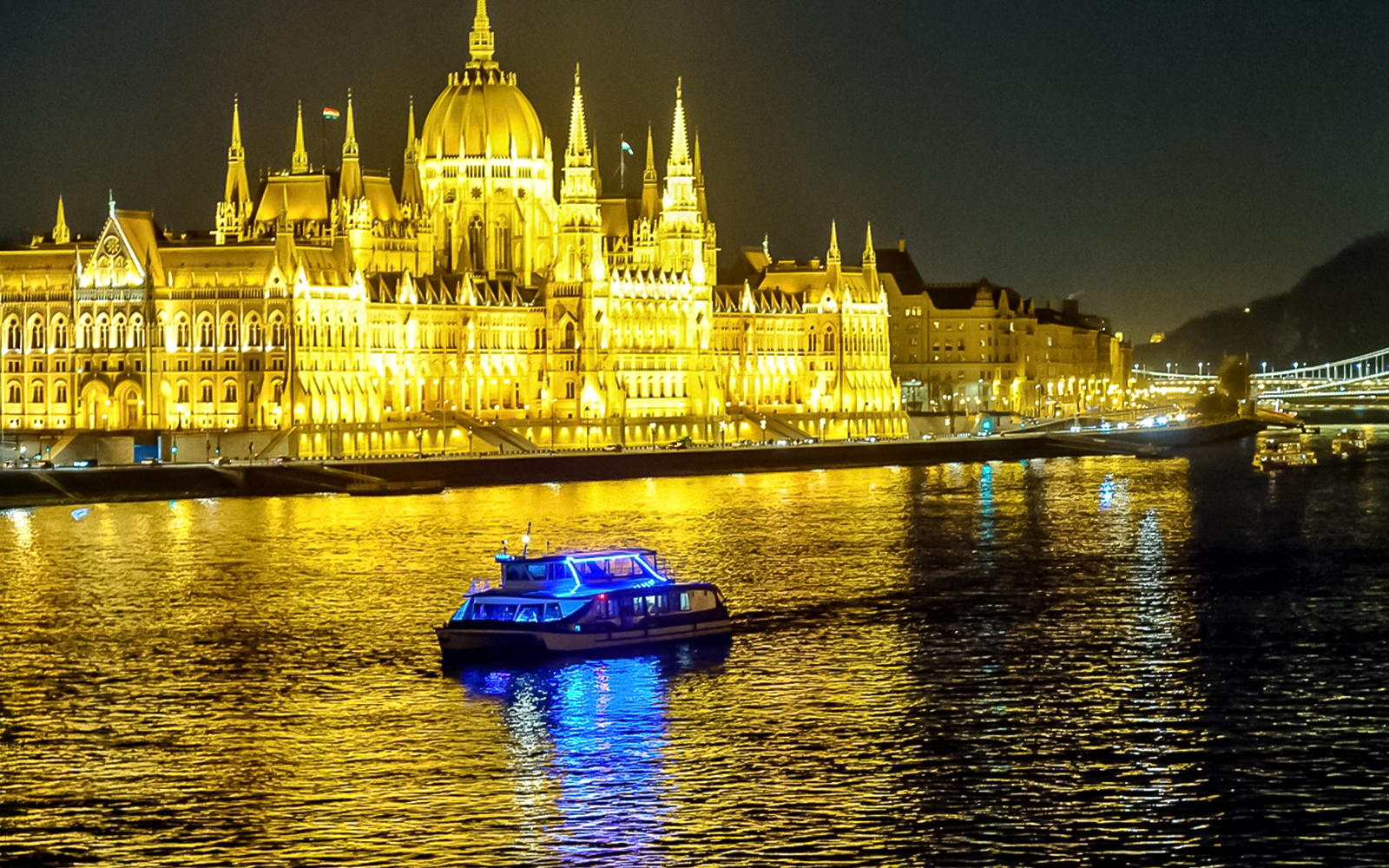 Cruise boat on Danube River with Budapest Parliament illuminated at night.