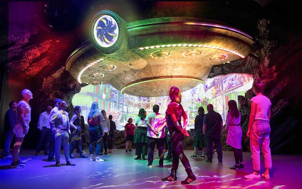 Visitors exploring Weta Workshop Unleashed exhibit in Auckland with colorful lights and sci-fi theme.