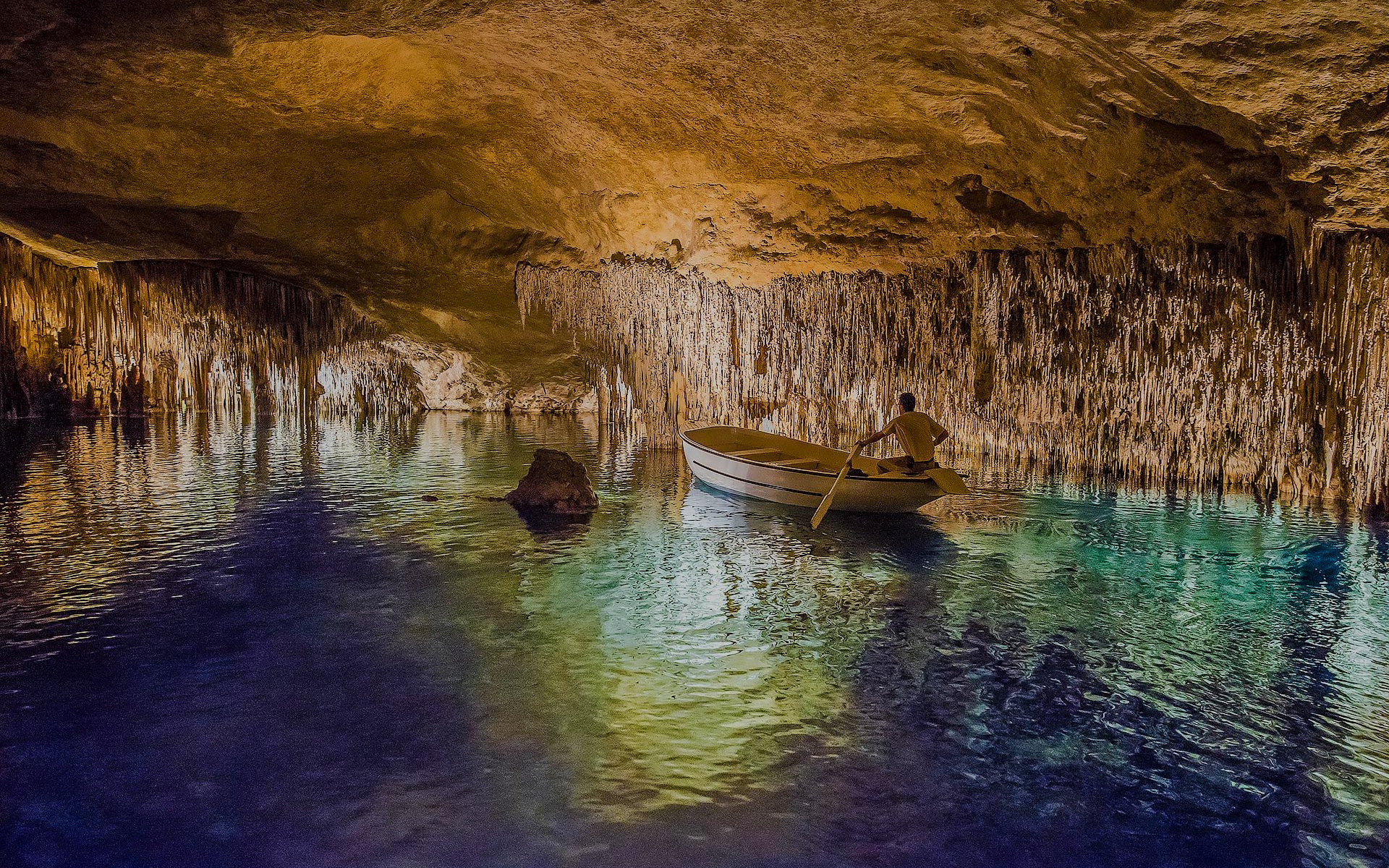 Boat tour inside Drach Caves with stalactites reflecting on the water.