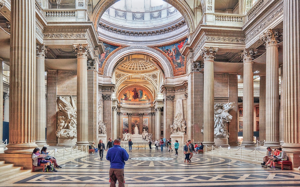 Interior of the Panthéon in Paris with visitors exploring the grand hall and sculptures.