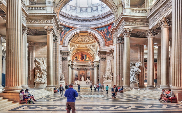 Interior of the Panthéon in Paris with visitors exploring the grand hall and sculptures.