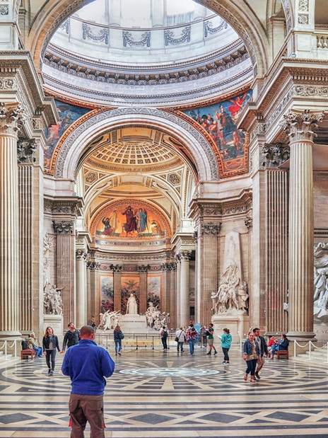 Interior of the Panthéon in Paris with visitors exploring the grand hall and sculptures.