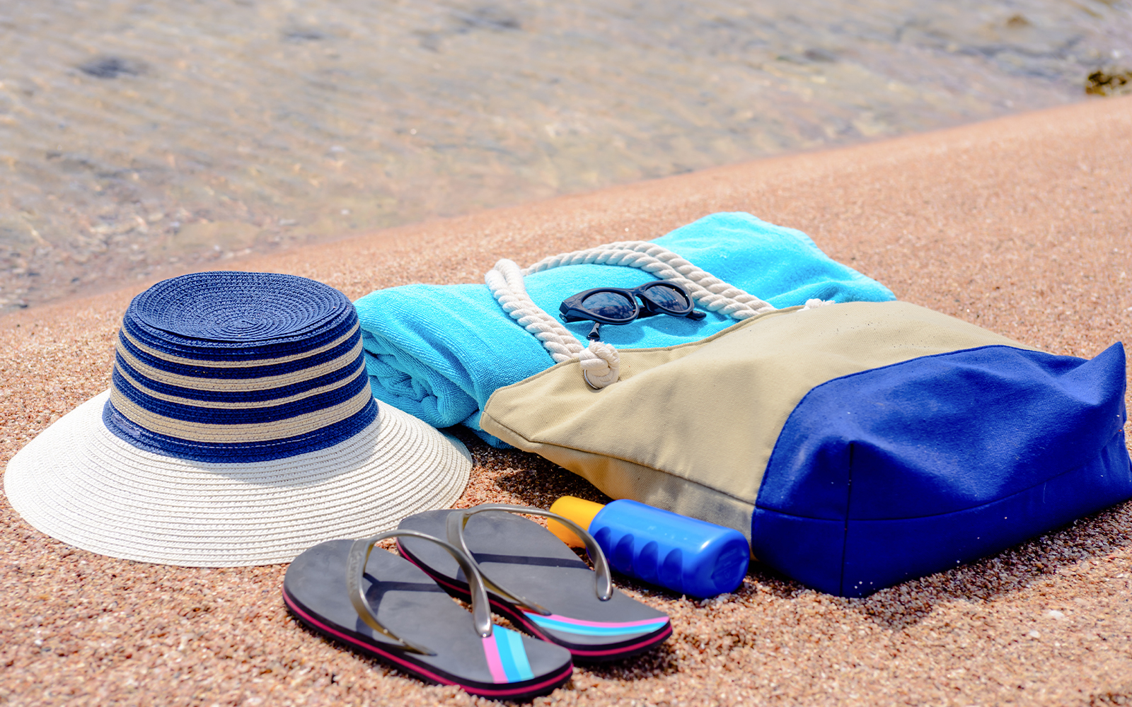 Beach essentials for snorkeling including a hat, towel, sunglasses, flip-flops, and sunscreen.