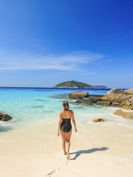 Tourist walking on sandy beach towards clear waters at Miang Island, Thailand.