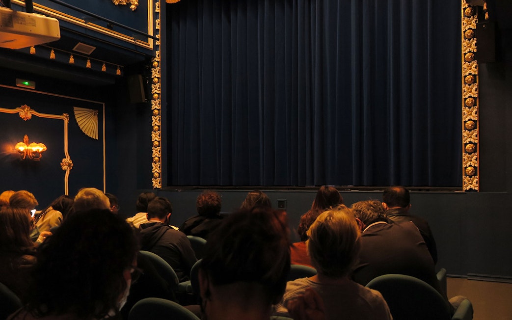 Audience seated at Triana Theater facing a closed stage curtain.