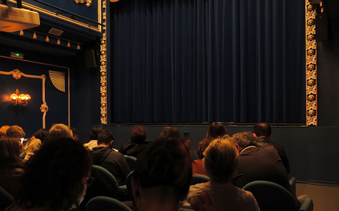 Audience seated at Triana Theater facing a closed stage curtain.