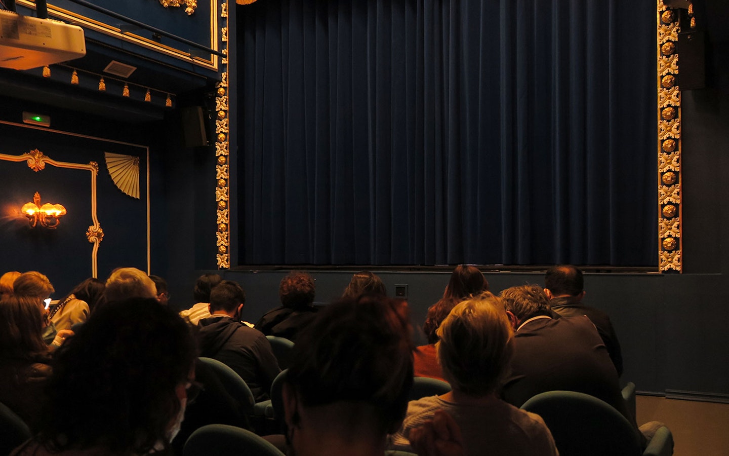 Audience seated at Triana Theater facing a closed stage curtain.