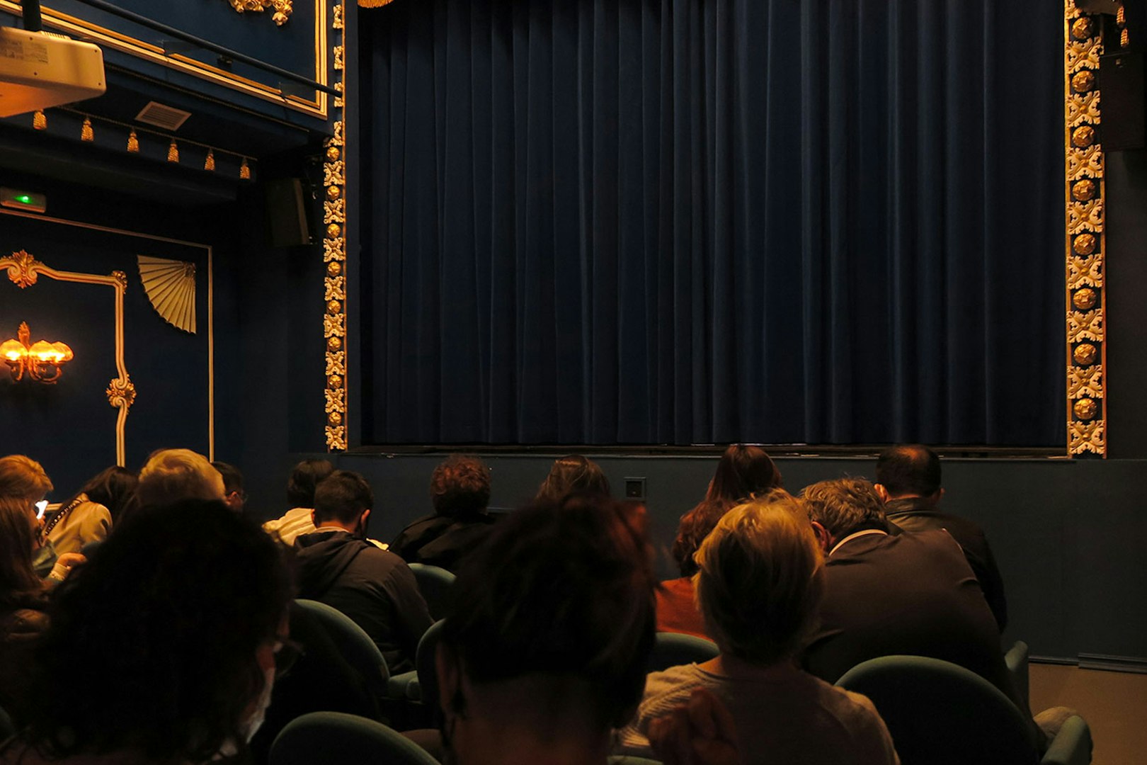 Audience seated at Triana Theater facing a closed stage curtain.
