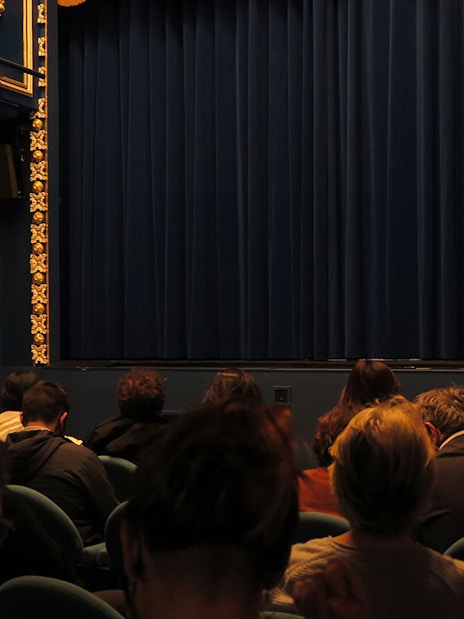 Audience seated at Triana Theater facing a closed stage curtain.