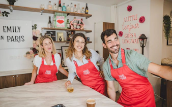 People enjoying Emily in Paris Croissant-Making Workshop, wearing red aprons in a kitchen setting.