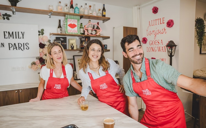 People enjoying Emily in Paris Croissant-Making Workshop, wearing red aprons in a kitchen setting.