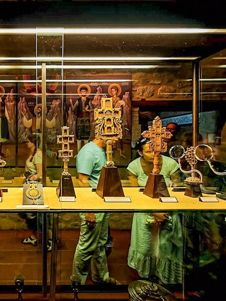 Visitors viewing religious artifacts in a Meteora monastery display case.