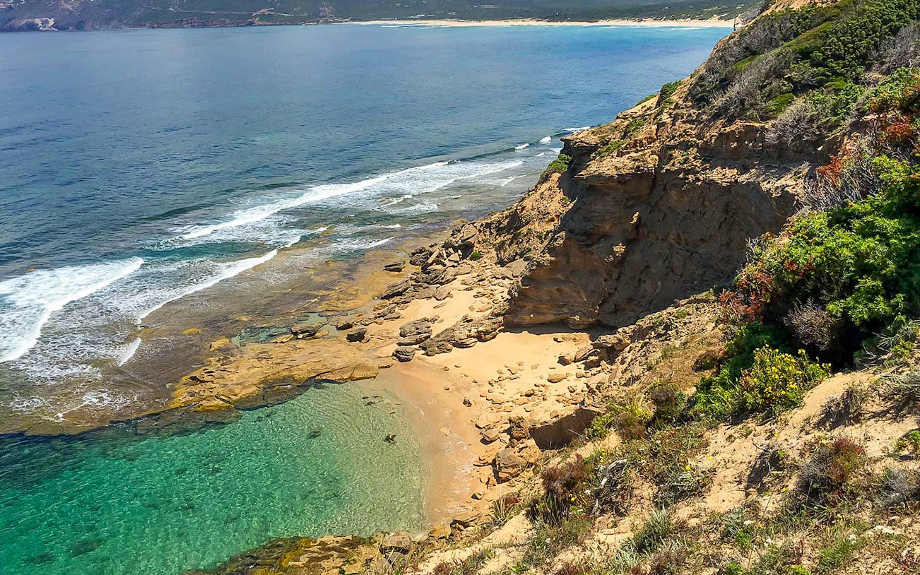 Coastal view along the Tonnare Trail from Portoscuso to Gonnesa, featuring rocky cliffs and clear sea.