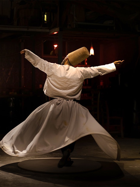 Sufi whirling dervish performing traditional dance in dimly lit room.