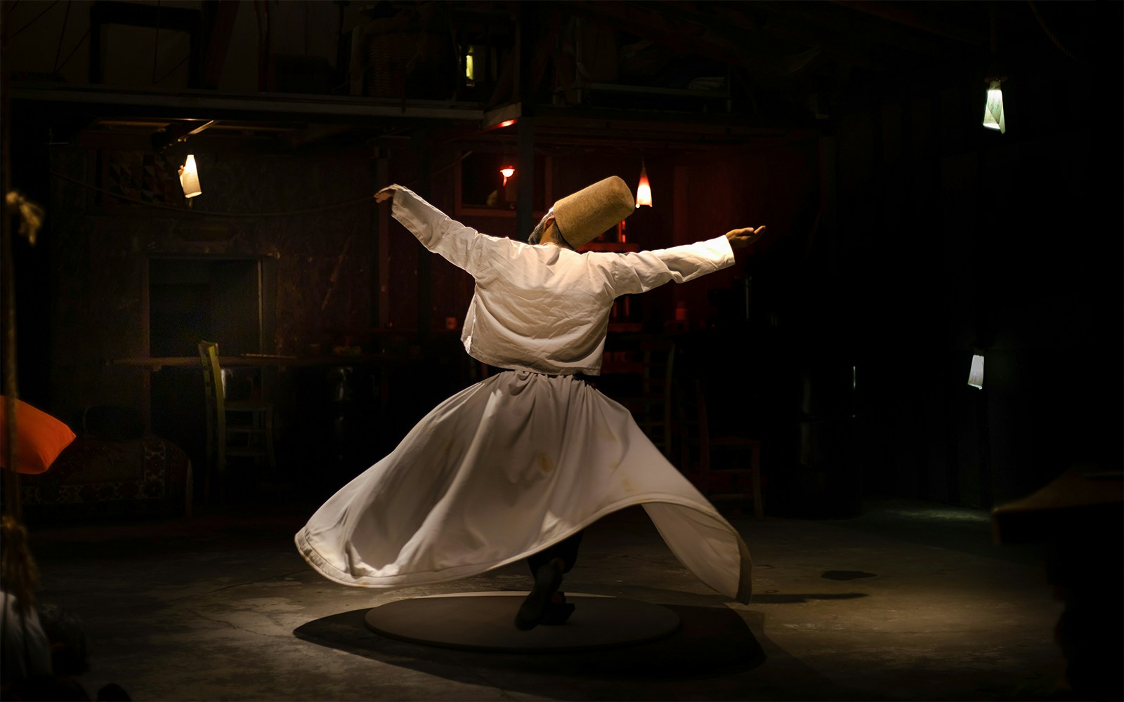 Sufi whirling dervish performing traditional dance in dimly lit room.