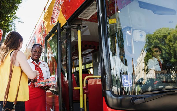 Tourist boarding Thessaloniki hop-on-hop-off bus with guide assisting.