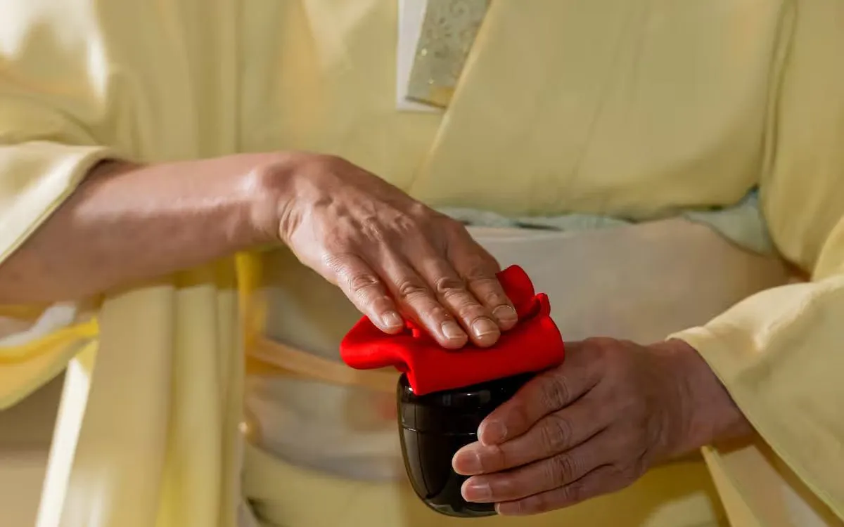 Hands preparing tea with a red cloth during a kimono tea ceremony in Shinjuku.