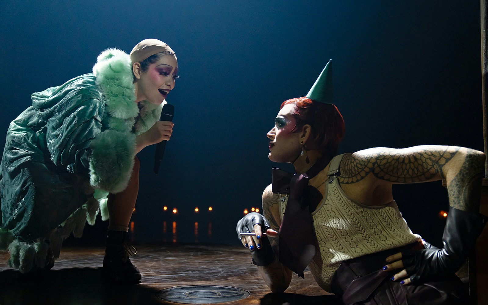 Performer in green coat singing to seated person in cabaret show.