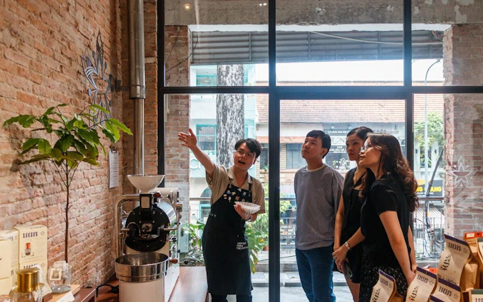 Tour guide explaining coffee roasting process to visitors in a Vietnamese café.