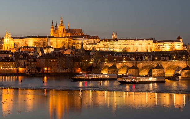Open-top glass boat on Vltava River with Prague Castle illuminated at night.