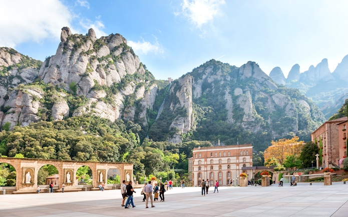 Visitors exploring Montserrat Monastery plaza with mountain backdrop in Catalonia, near Barcelona.