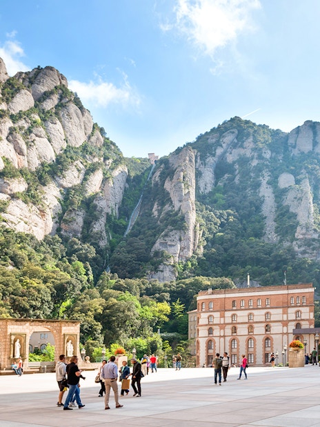 Visitors exploring Montserrat Monastery plaza with mountain backdrop in Catalonia, near Barcelona.