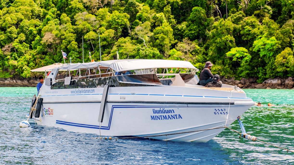 Speedboat anchored near lush Surin Islands, Thailand, with passengers on deck.