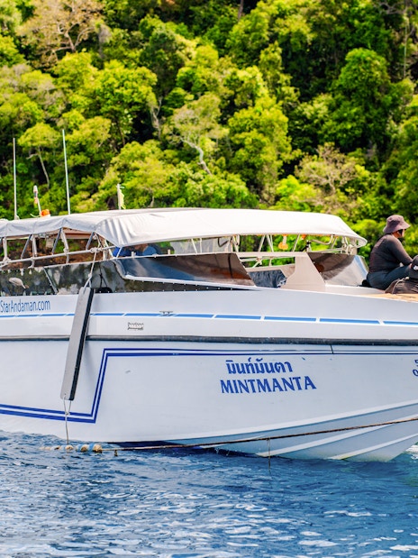 Speedboat anchored near lush Surin Islands, Thailand, with passengers on deck.