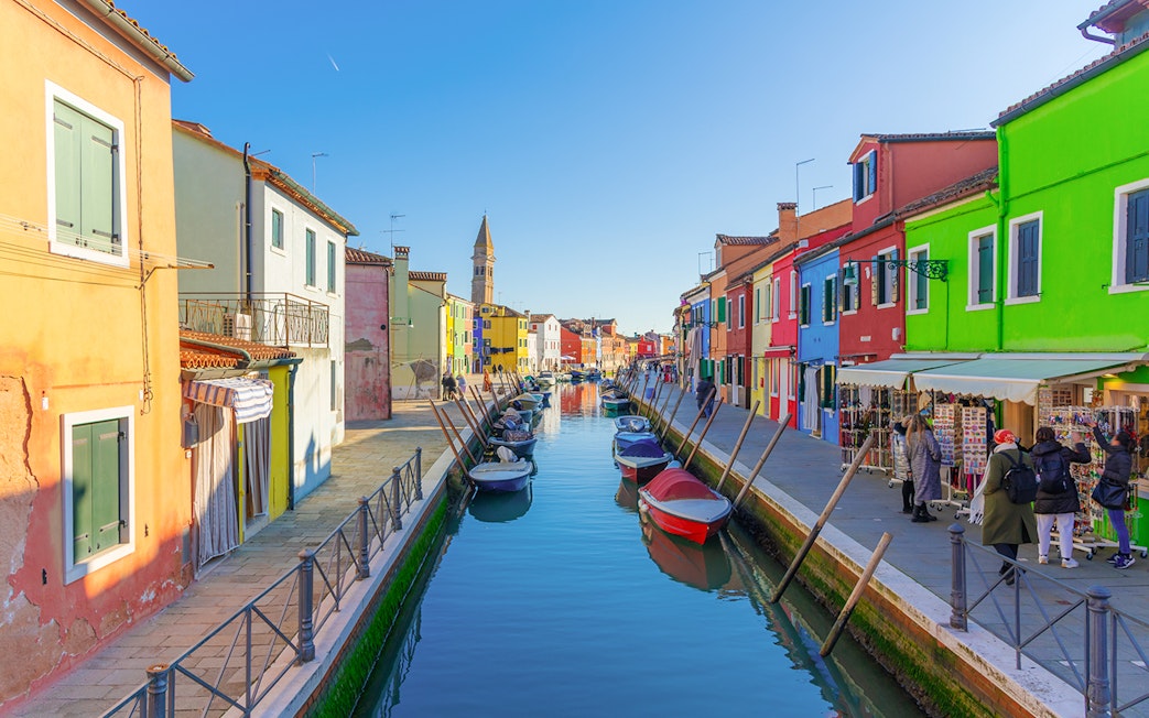 Colorful buildings along Burano canals with boats and tourists exploring.