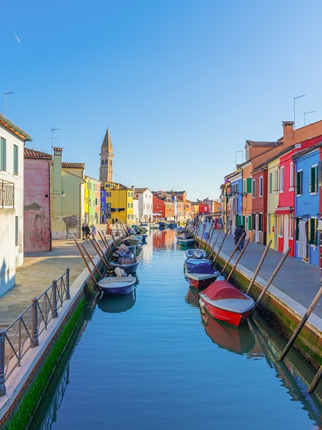 Colorful buildings along Burano canals with boats and tourists exploring.