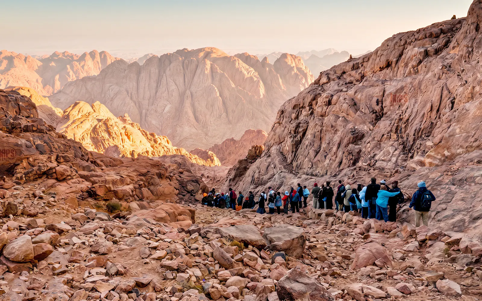 Group hiking on rocky trail at Mount Sinai during sunrise.