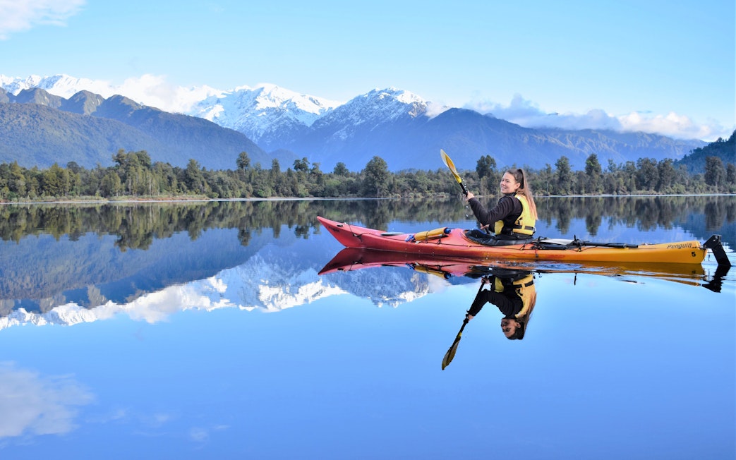 Girl kayaking on Lake Mapourika with snow-capped mountains in the background.