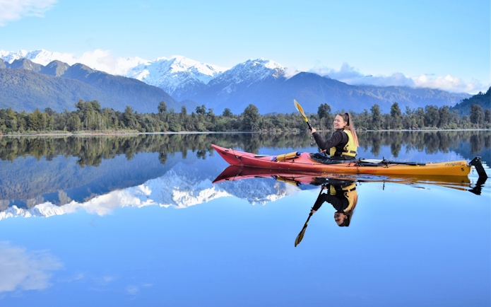 Girl kayaking on Lake Mapourika with snow-capped mountains in the background.