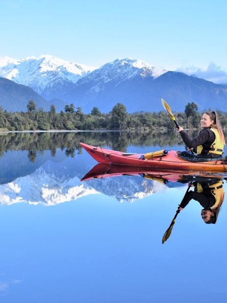 Girl kayaking on Lake Mapourika with snow-capped mountains in the background.