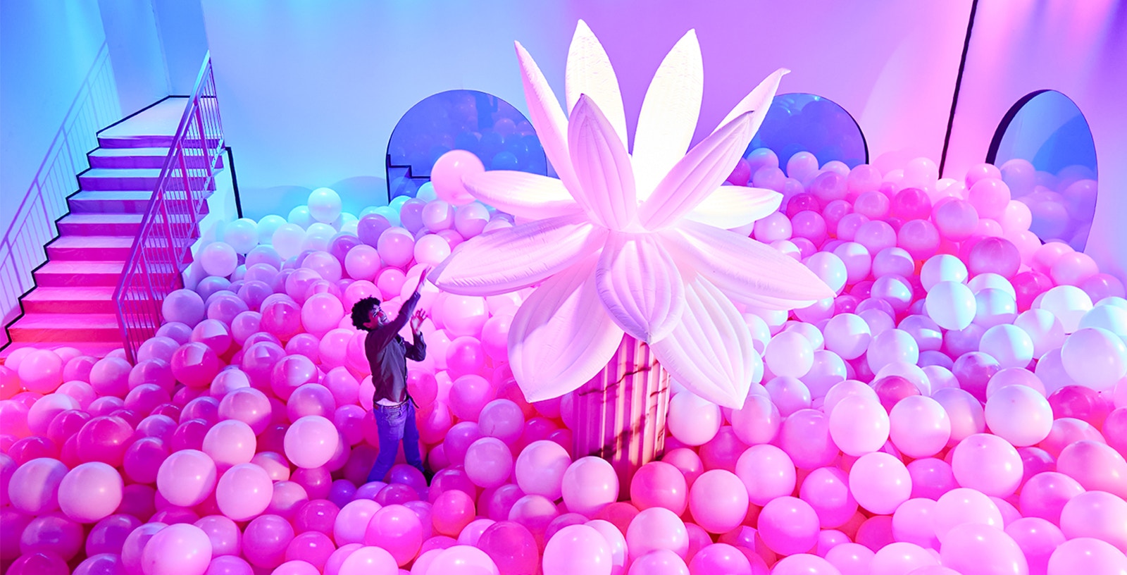 Person exploring pink balloon room with large flower at Bubble Planet, Seattle.