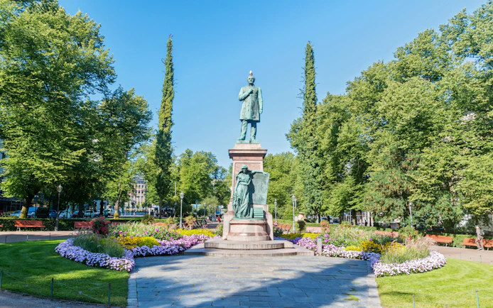 Statue of Johan Ludvig Runeberg in Esplanadi park, Helsinki, surrounded by trees and flowers.