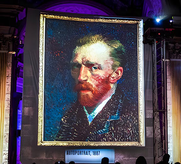 Van Gogh self-portrait at London exhibition with guests viewing.