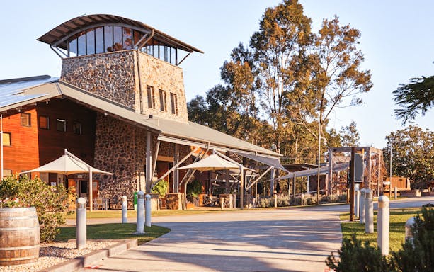 Winery building with stone facade and outdoor seating area surrounded by trees.