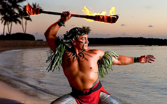 Fire dancer performing at sunset on the beach at Paradise Cove Luau, Hawaii.
