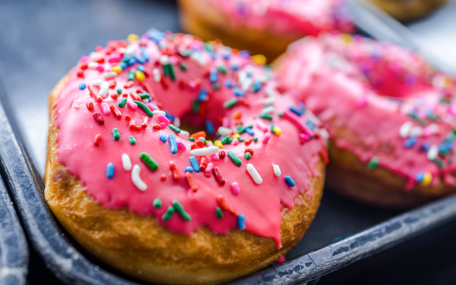 Pink iced donuts with rainbow sprinkles on a white plate.