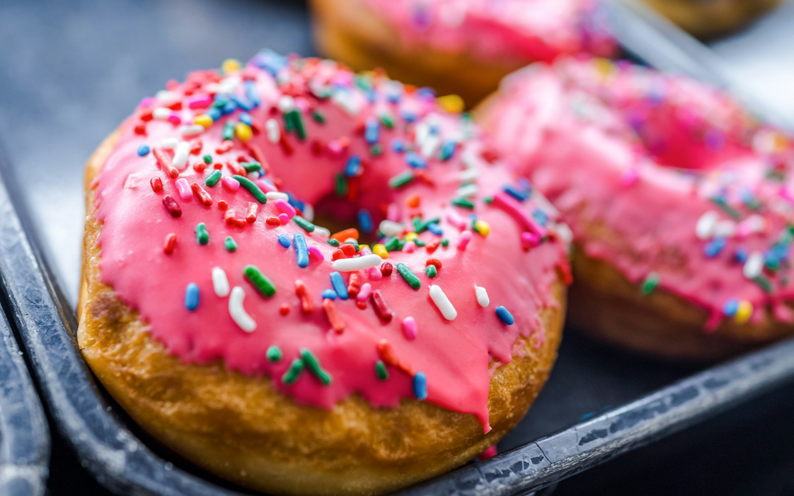 Pink iced donuts with rainbow sprinkles on a white plate.
