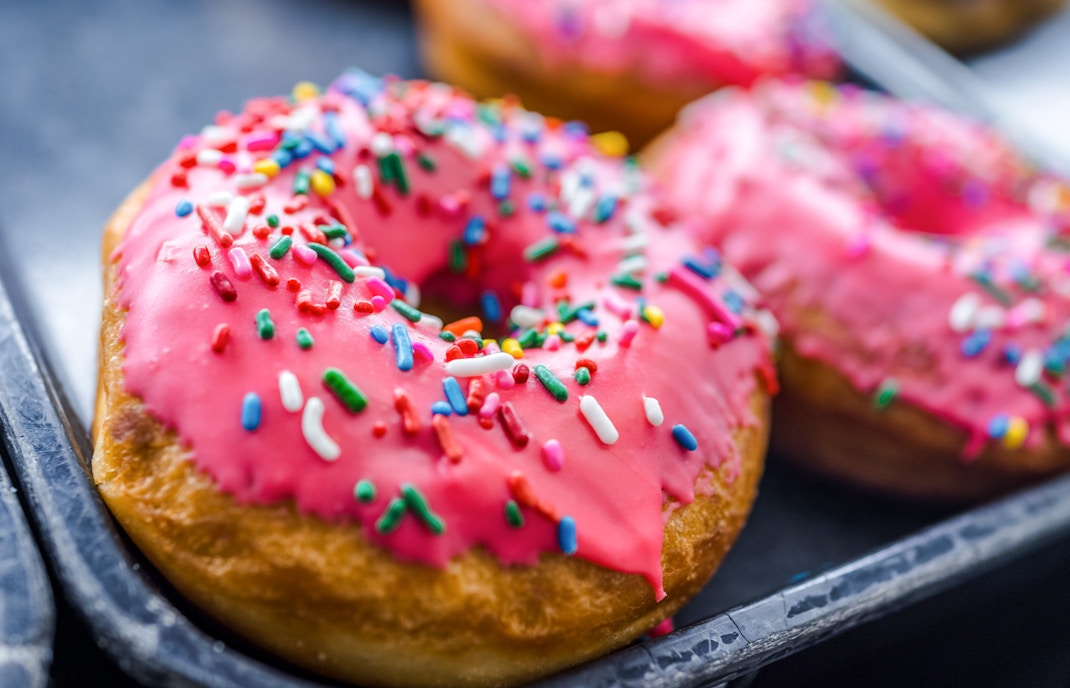Pink iced donuts with rainbow sprinkles on a tray.
